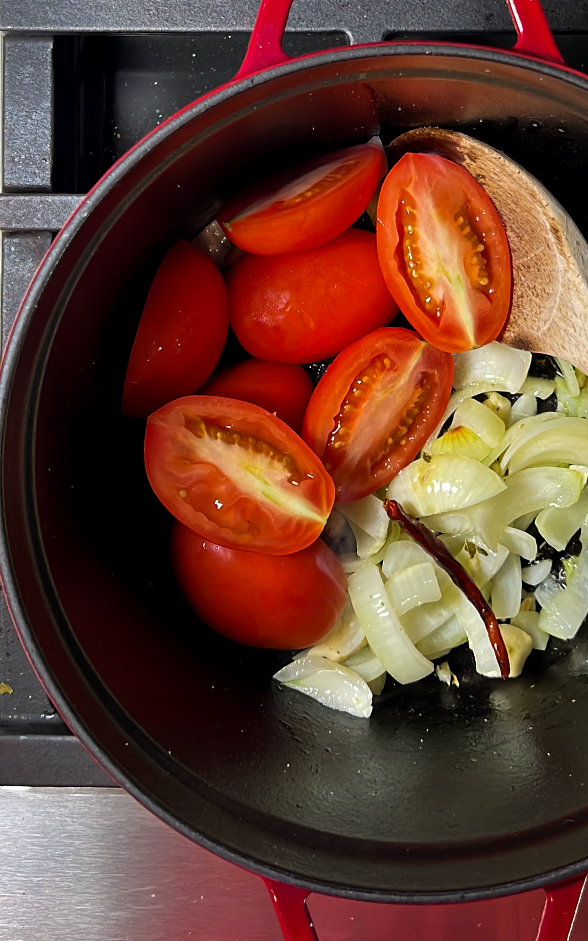 Tomates partidos por la mitad y cebollas en rodajas en una olla roja, listos para cocinar sopa de calabaza.