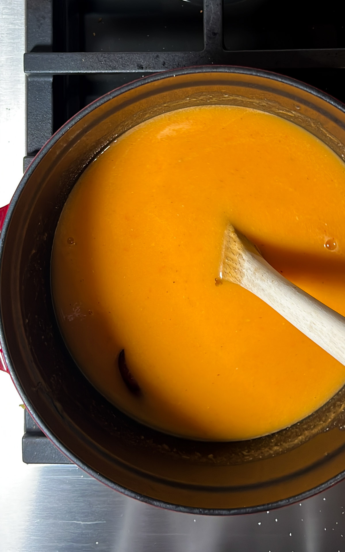 Olla de sopa de calabaza con una cuchara de madera revolviendo sobre una estufa.