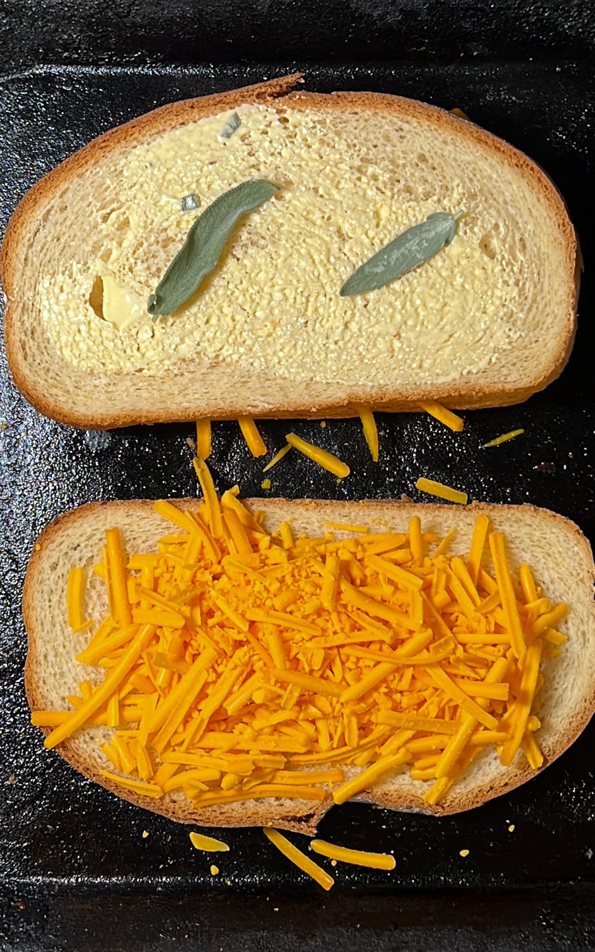 Dos rebanadas de pan en una sartén, una cubierta con mantequilla y hojas de salvia y la otra con queso cheddar rallado, servidas junto con sopa de calabaza.