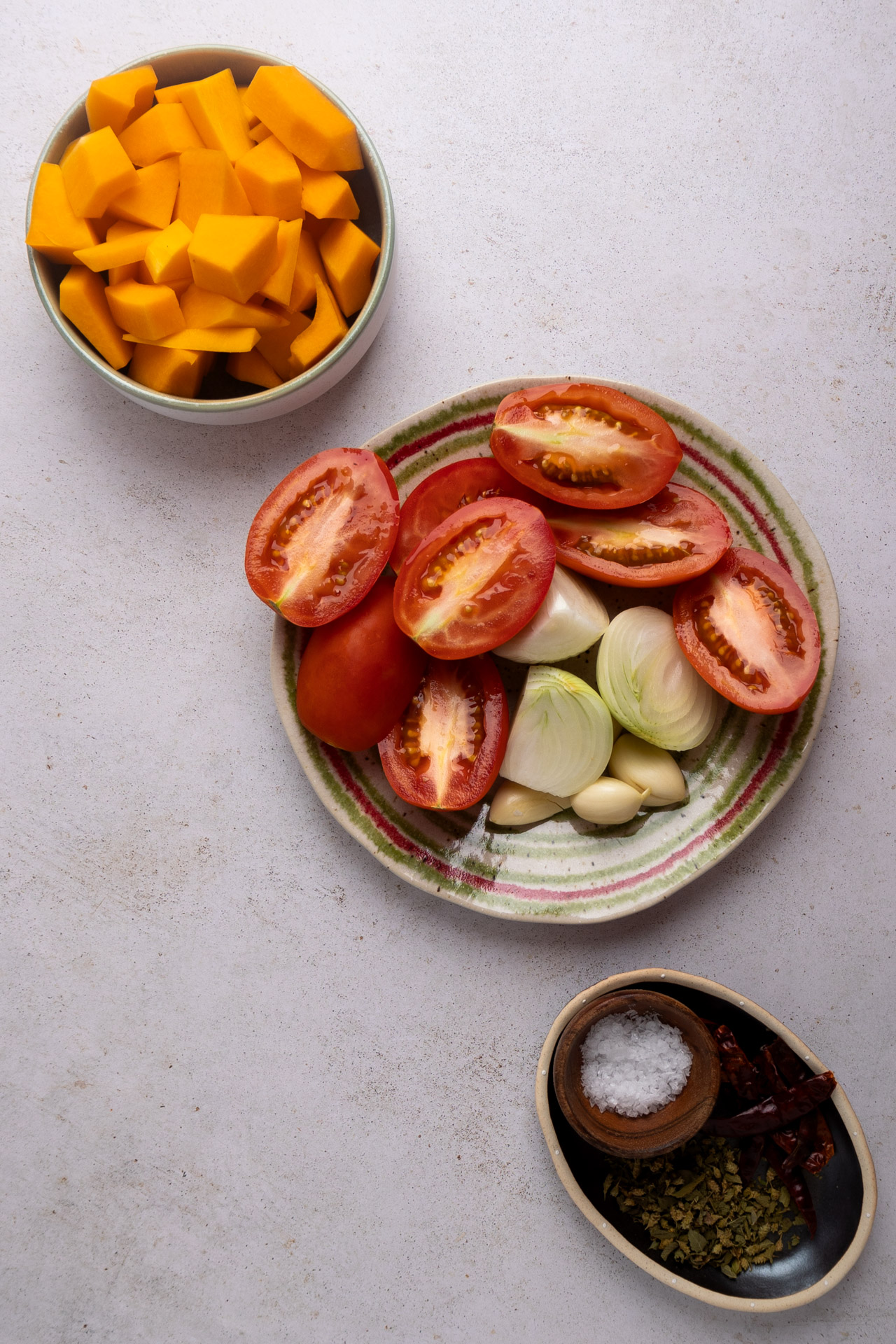 Vista de arriba hacia abajo de los ingredientes en la encimera de la cocina, incluidos tomates en rodajas, cebollas, ajo, mango cortado en cubitos, sopa de calabaza y un plato de especias y sal.