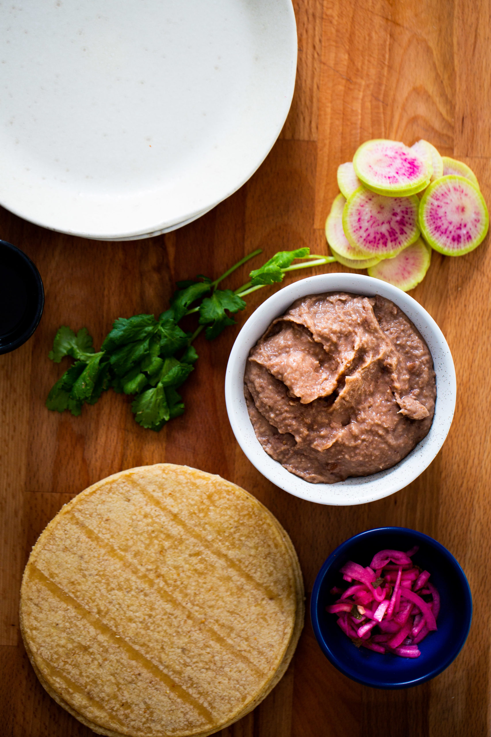 Tazón con frijoles, tortillas de maíz, un tazón con cebolla morada.