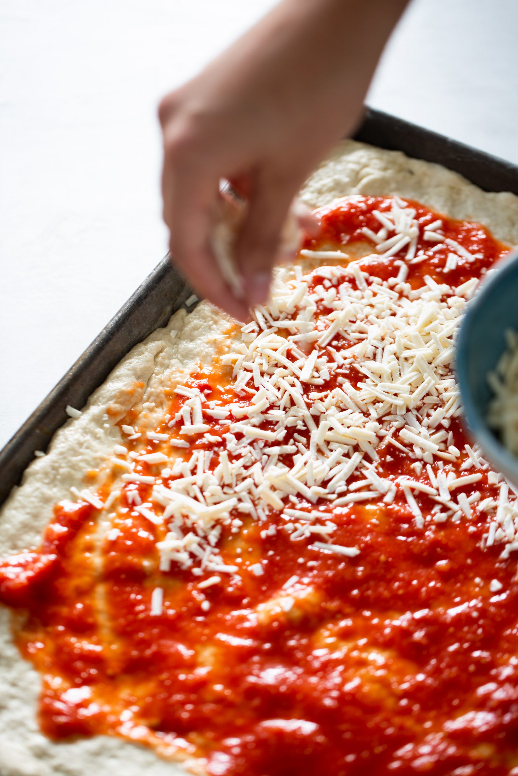 Poniéndole queso a una pizza en charola, sheet pan pizza