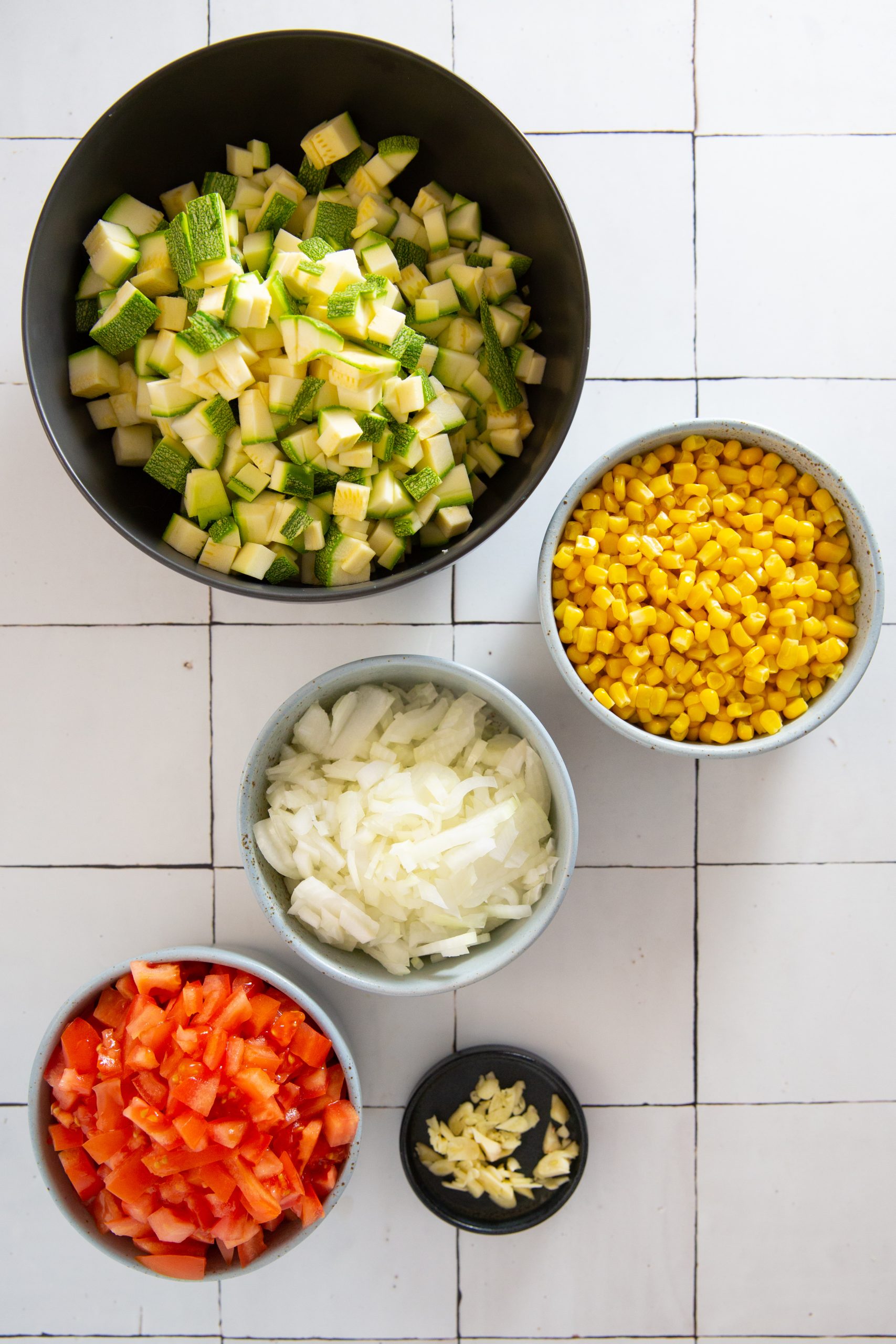 tazón con calabacitas, tazón con elote, cebolla, tomate picado y ajo.