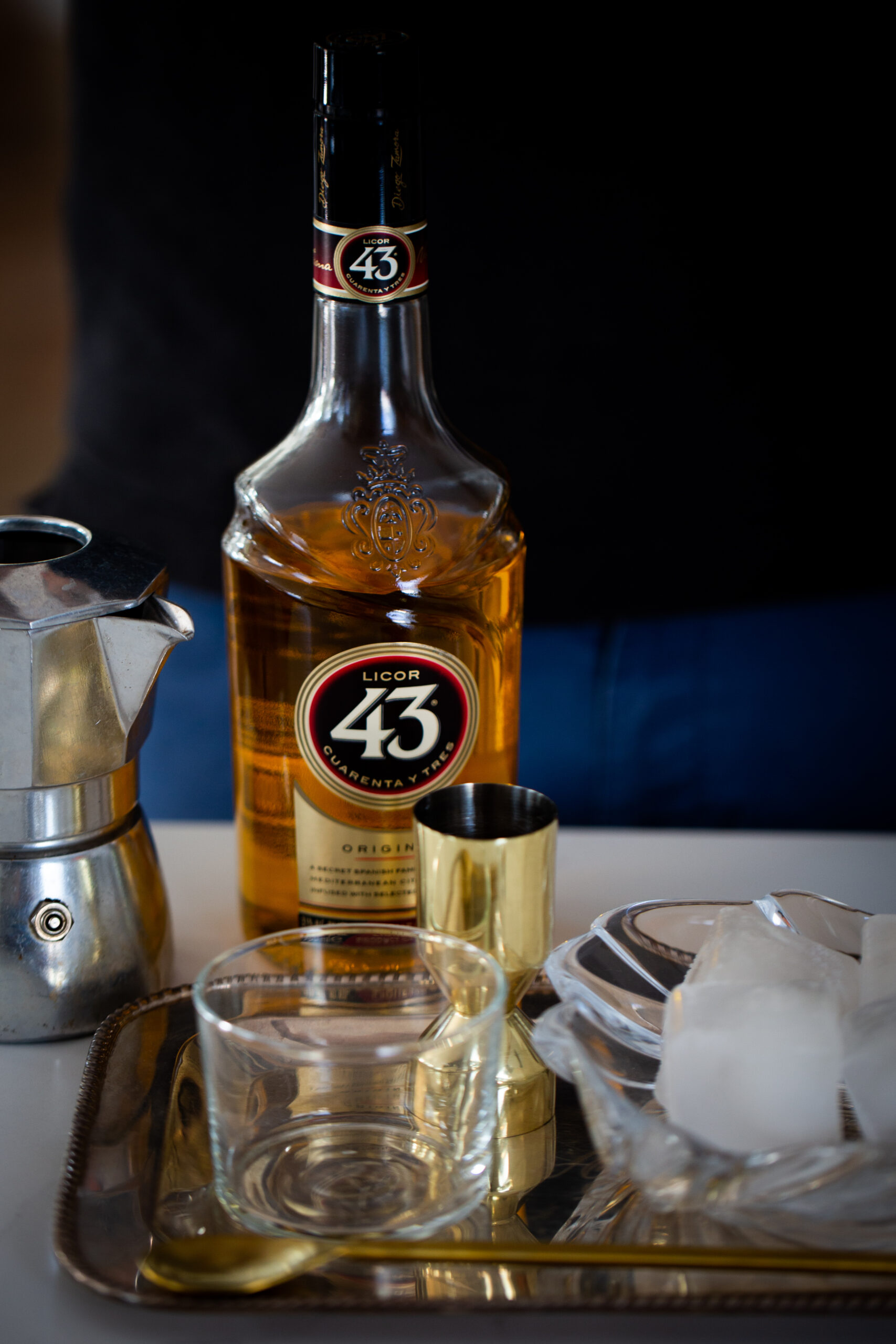 Una botella de licor 43 junto una charola con vaso y hielo y una cafetera de espresso