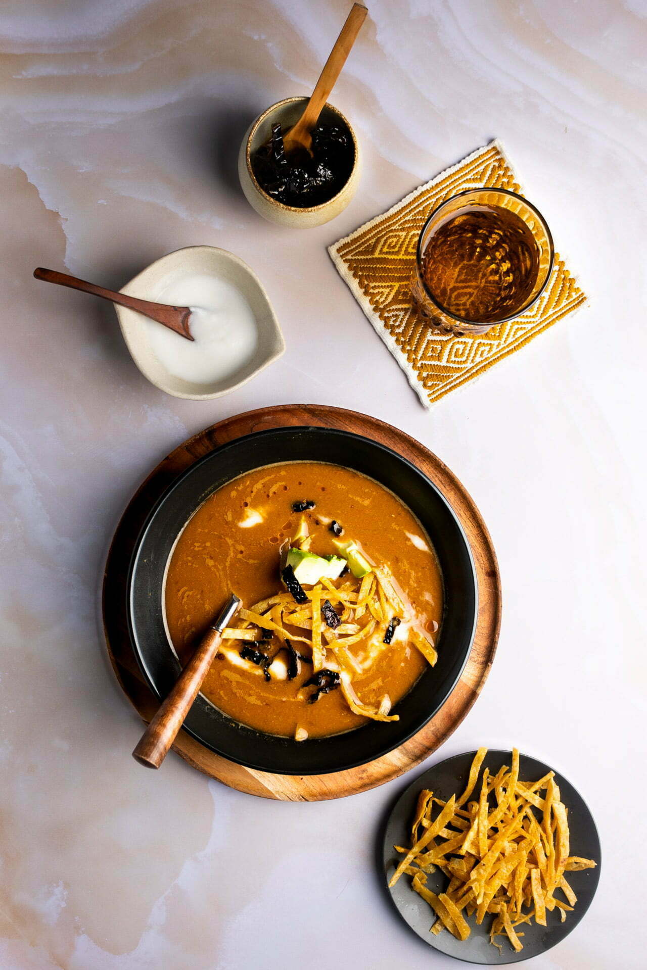 sopa de frijol pinto servida en un plato negro y con tortillas fritas, chile ancho y aguacate encima