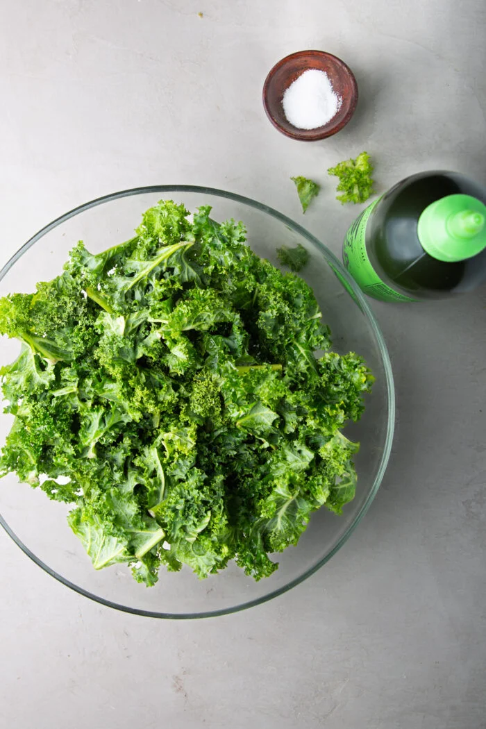 kale en una ensaladaera de vidrio, una botella de aceite de oliva y sal.