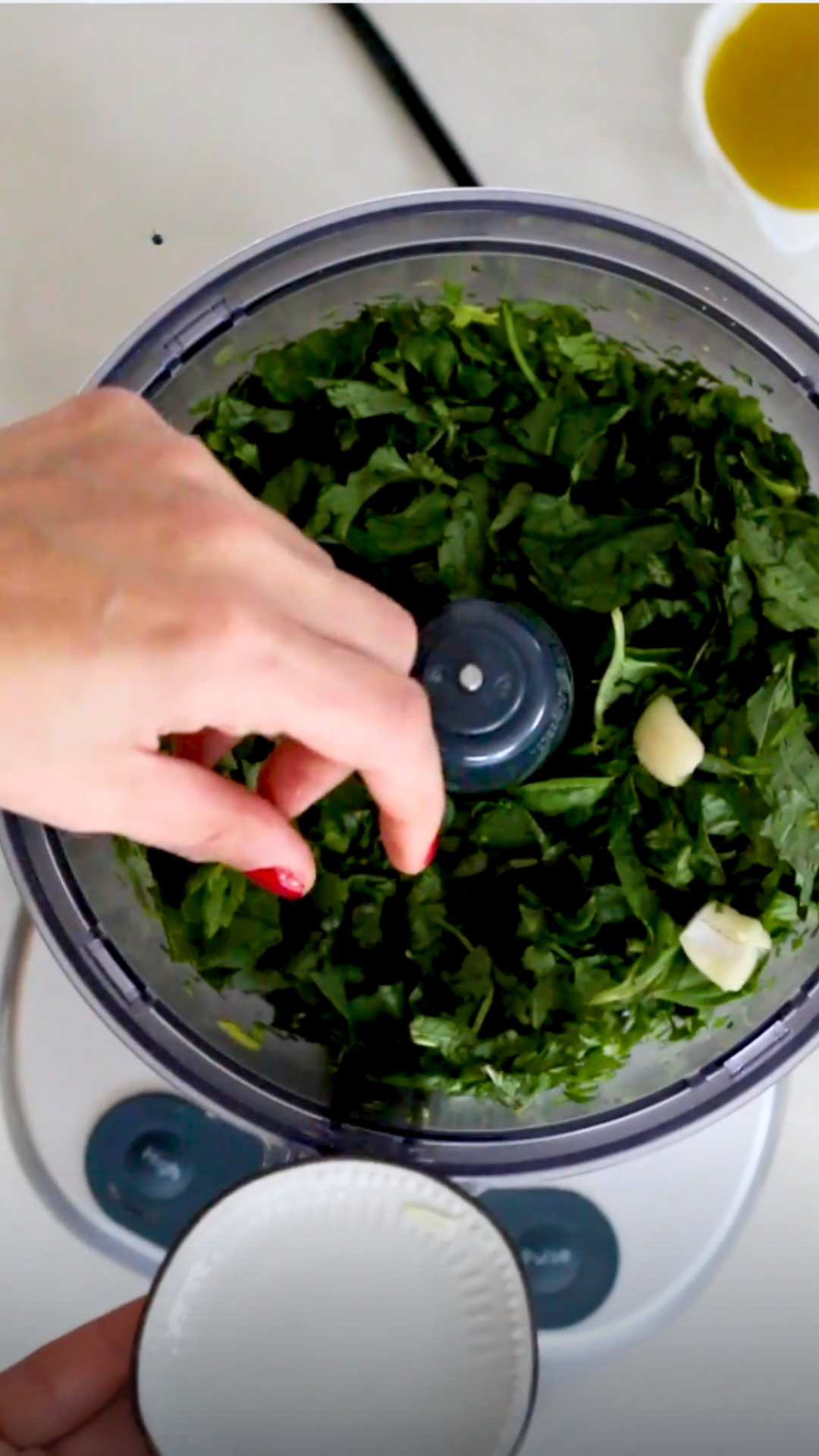 A person is blending greens in a food processor to make vegan pesto.