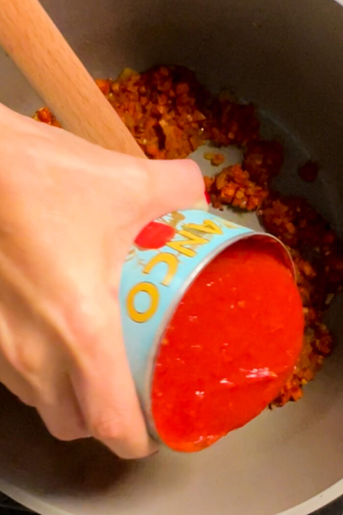 Una persona vegana echando salsa de tomate en una sartén.