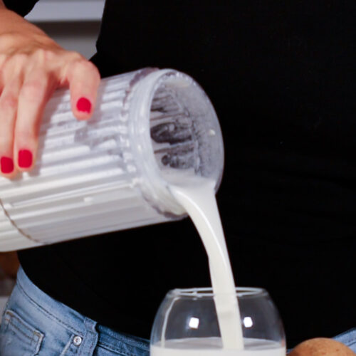 Una mujer vierte leche en un vaso para preparar la mejor crema espesa vegana casera.