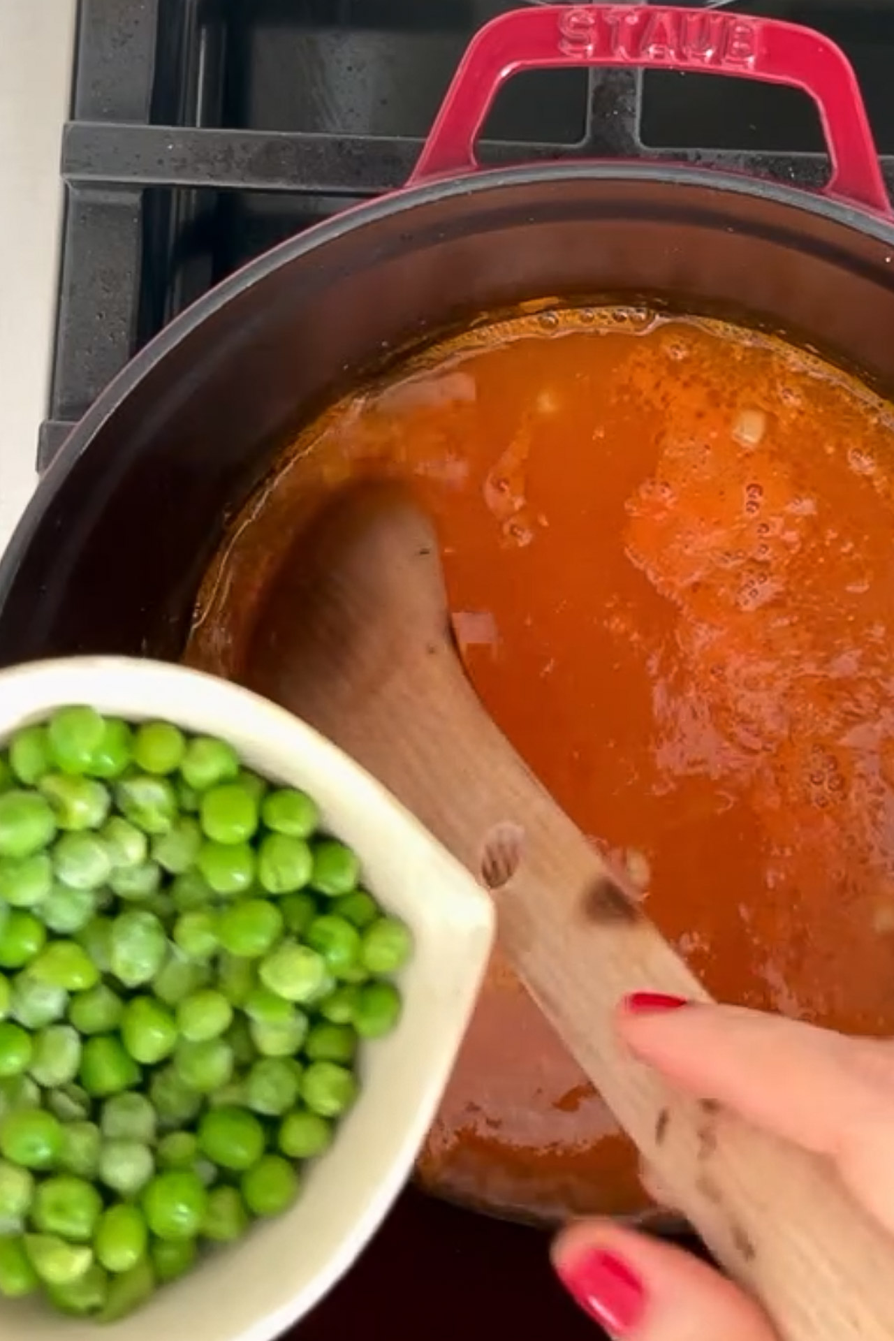 Una persona remueve fácilmente guisantes sanos en una olla al fuego para preparar Sopa De Verduras.