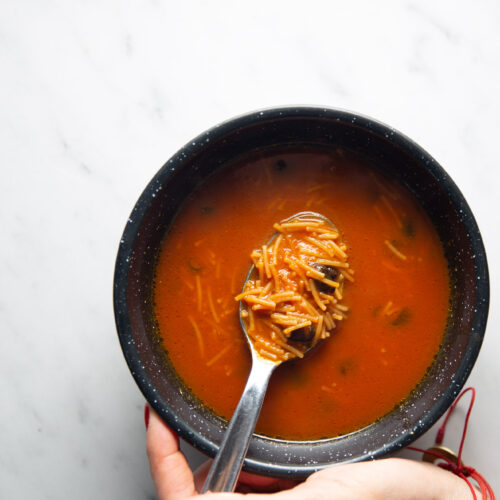 Una persona sostiene un cuenco de sopa con una cuchara, disfrutando de una ración caliente de Sopa de Fideo.