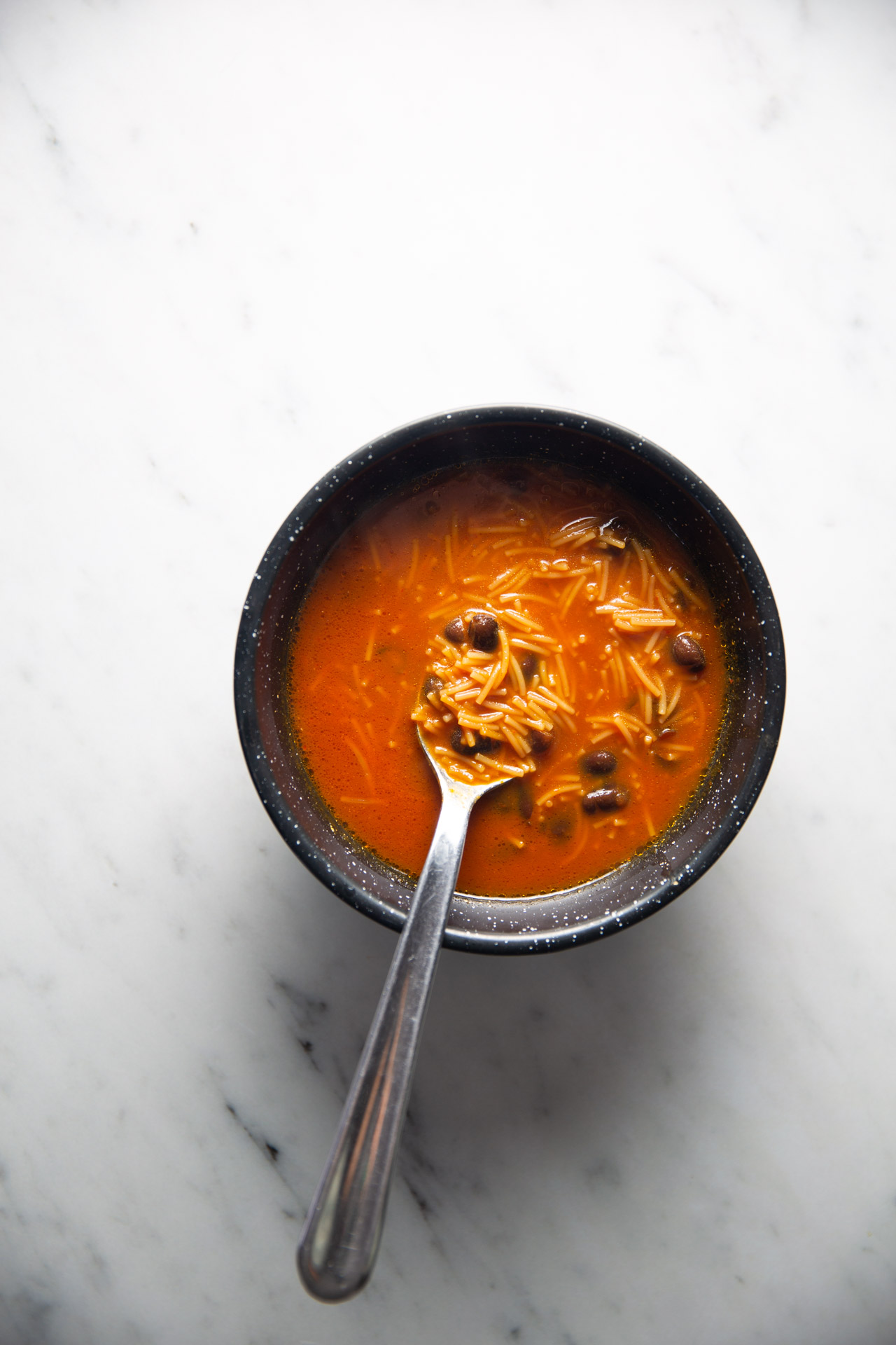 Un cuenco de sopa de fideo y frijol con una cuchara dentro.