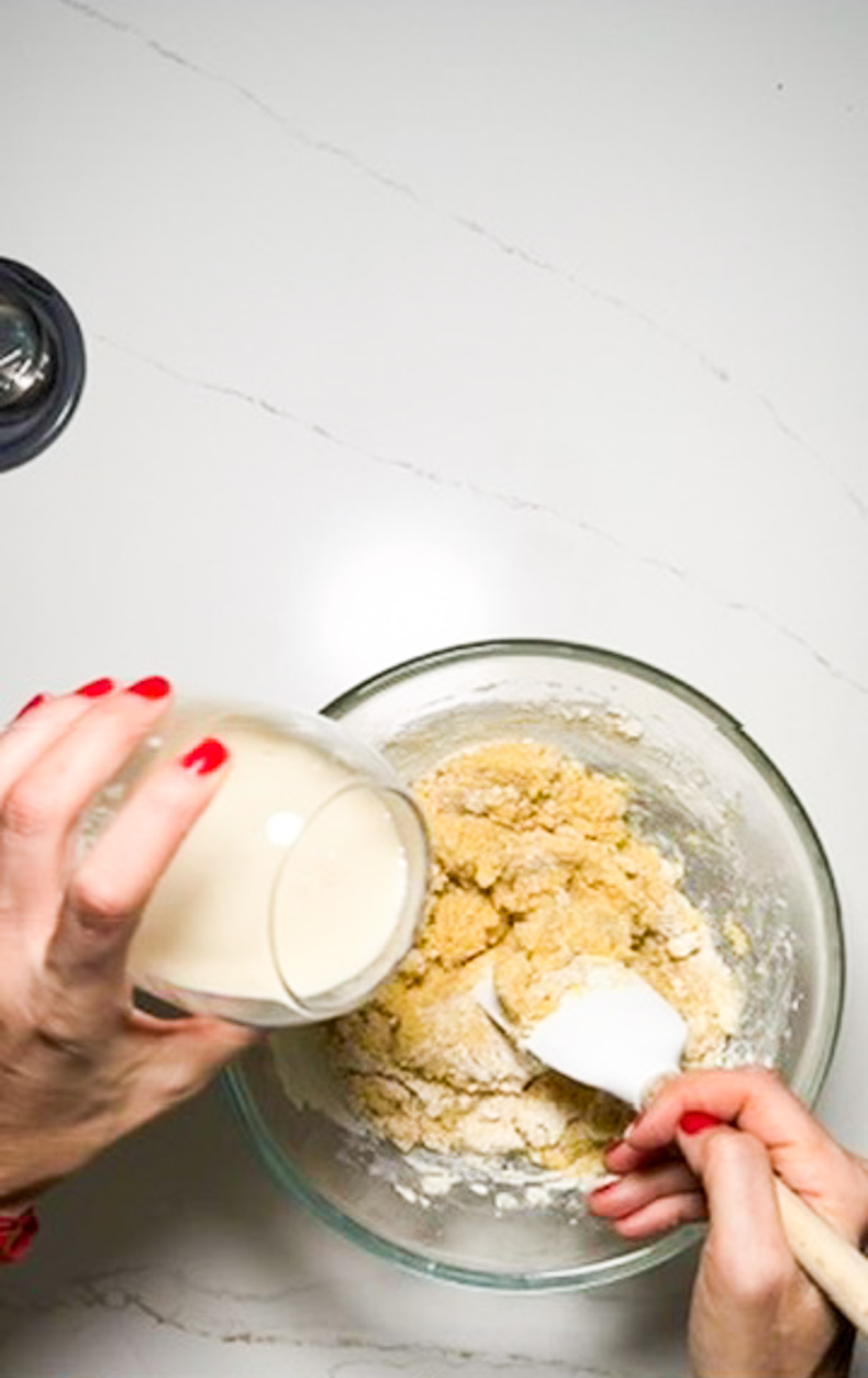 Una mujer vegana vierte leche en un bol de masa para una receta de pan de maíz.