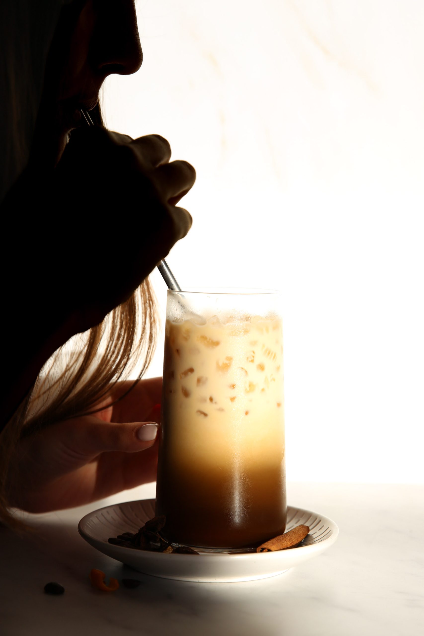 A woman enjoying an iced latte from a glass.