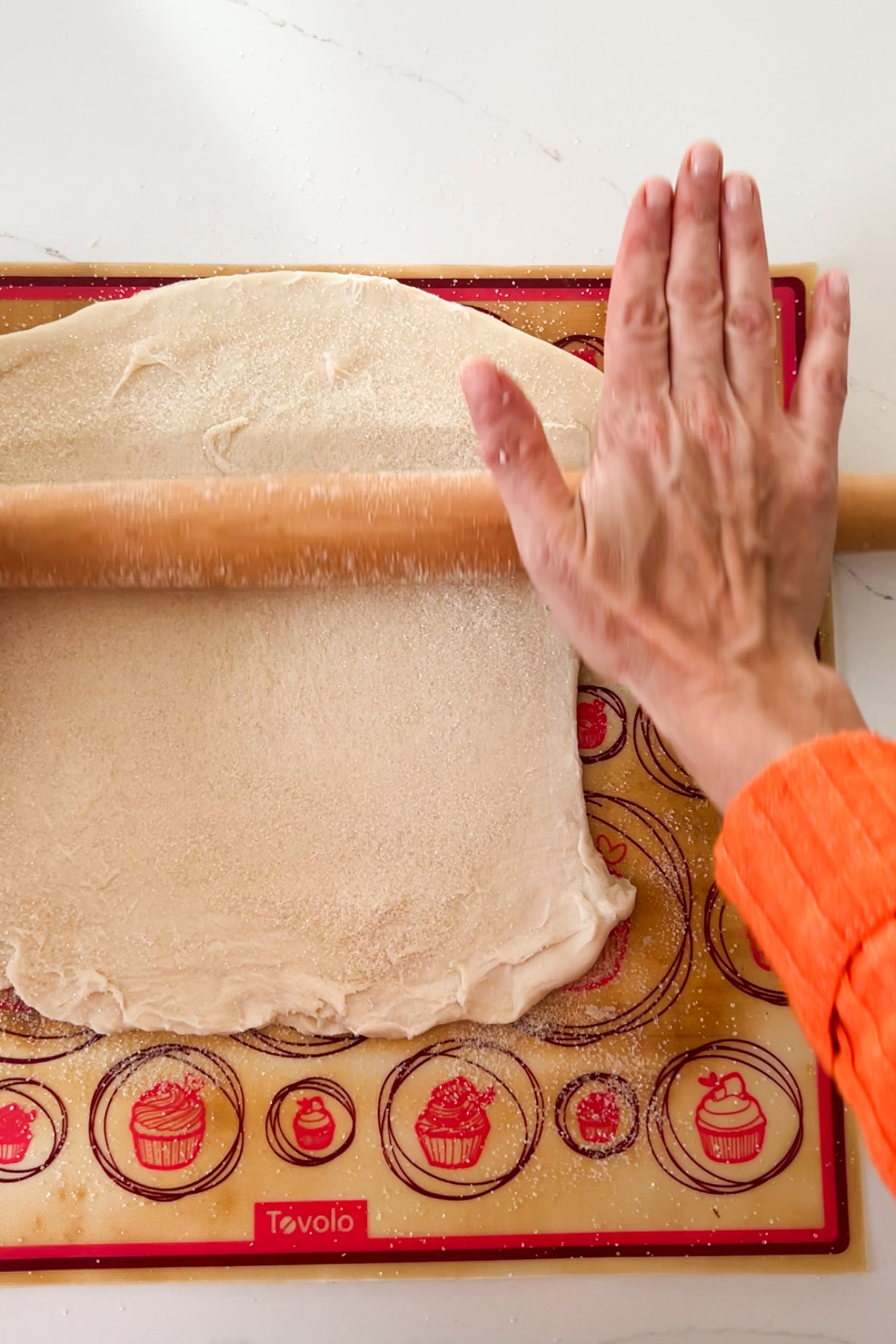 A person rolling out dough for Pan Dulce, a vegan recipe, on a baking sheet.