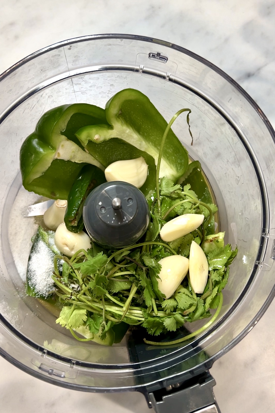 Un procesador de alimentos lleno de pimientos verdes, ajo y cilantro.