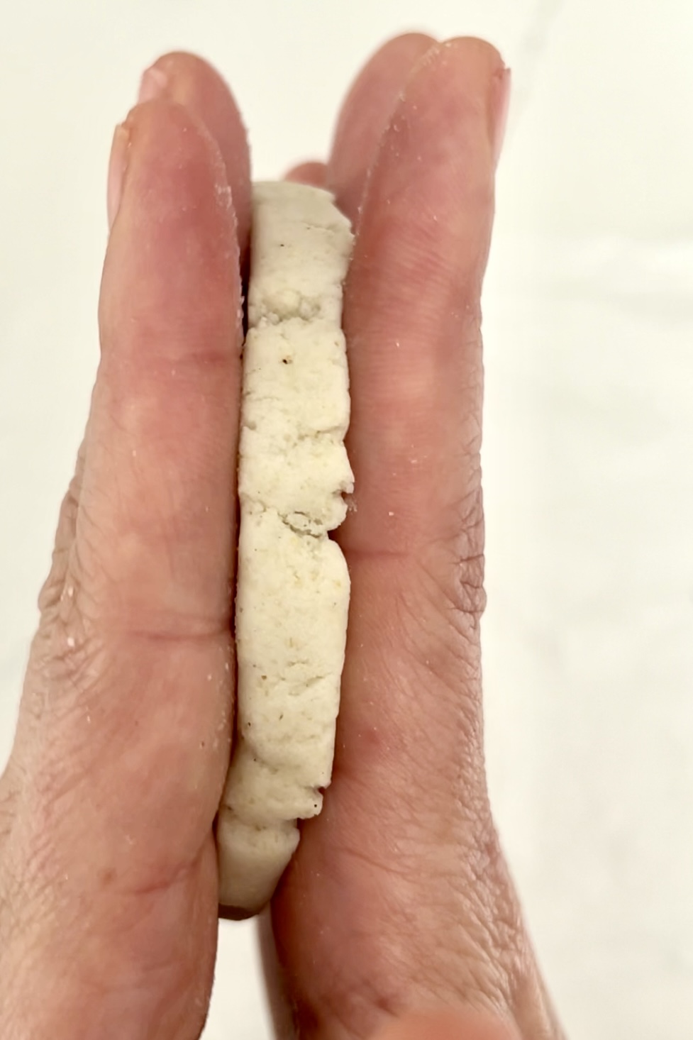 Una mano que sostiene un sope pequeños, redondos y blancos entre dos dedos.
