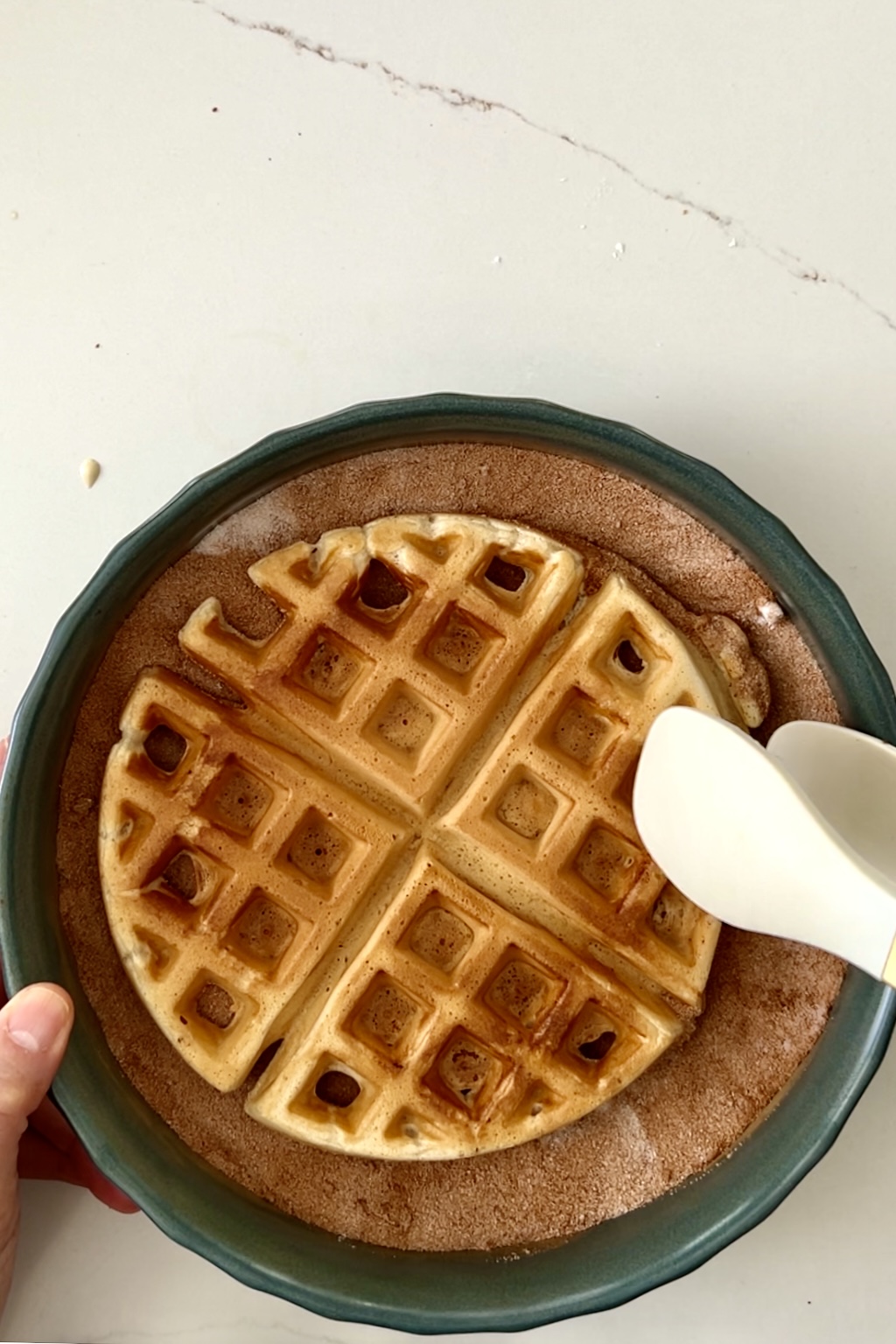 a waffle being coated in a sugar-cinammon mix